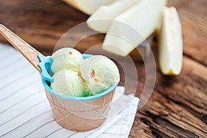 Vanilla ice cream with a taste of melon in a bowl on old wooden table. On the background of sliced fresh melon