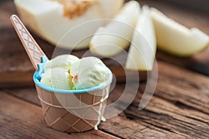 Vanilla ice cream with a taste of melon in a bowl on old wooden table. On the background of sliced fresh melon