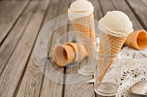 Vanilla ice cream in waffle cone on rustic wooden background