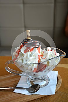 Fresh strawberries and vanilla ice cream with whipped cream on a glass bowl.