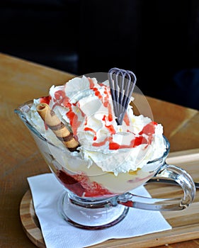 Vanilla ice cream and whipped cream with hot strawberries on a glass bowl.