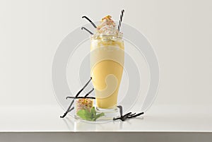 Vanilla milkshake with cream decorated with branch vanilla on table