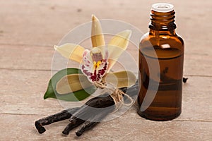 Vanilla pods, aromatherapy oil and orchid flowers on wooden back photo