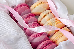 vanilla and raspberry macaroons in a box on a white napkin with a pink ribbon