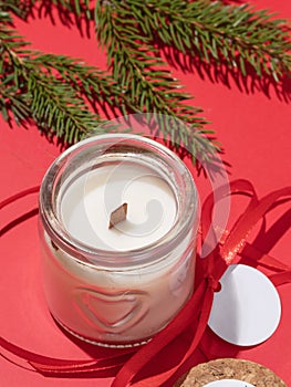 Vanilla scented candle in an open glass jar and a fir branch on a red background