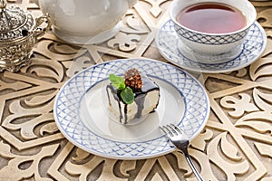 Vanilla souffle with dark chocolate glaze and cup of tea on orientabl wooden table