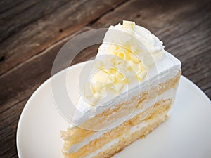 Vanilla sponge cake with cream and white chocolate decorate. Sliced piece of cake on white plate. Served on wooden table.