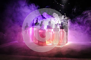 Vape concept. Smoke clouds and vape liquid bottles on dark background. Light effects.