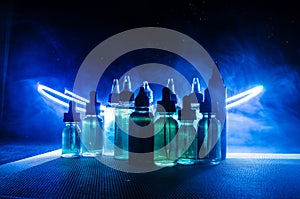 Vape concept. Smoke clouds and vape liquid bottles on dark background. Light effects.