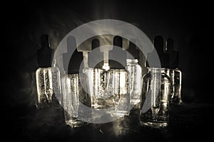 Vape concept. Smoke clouds and vape liquid bottles on dark background. Light effects. Useful as background or vape advertisement.