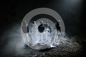 Vape concept. Smoke clouds and vape liquid bottles on dark background. Light effects. Useful as background or vape advertisement.