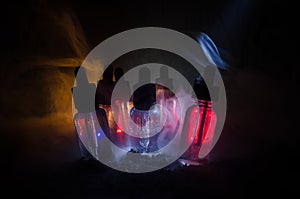 Vape concept. Smoke clouds and vape liquid bottles on dark background. Light effects. Useful as background or vape advertisement.