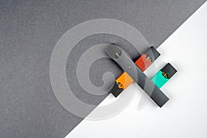 Vaping device and colored vaping pods on grey and white diagonal background.