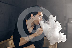 Vaping man holding a mod. A cloud of vapor. Black background.