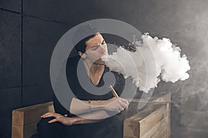 Vaping man holding a mod. A cloud of vapor. Black background.