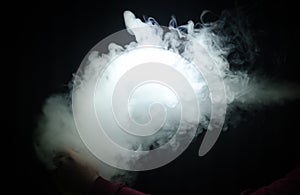 Vaping man holding a mod. A cloud of vapor. Black background. Vaping an electronic cigarette with a lot of smoke