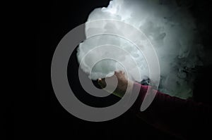Vaping man holding a mod. A cloud of vapor. Black background. Vaping an electronic cigarette with a lot of smoke