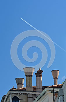 A vapour trail in a blue sky, above some chimneys