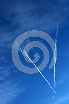 Vapour trails in blue sky with touches of white clouds