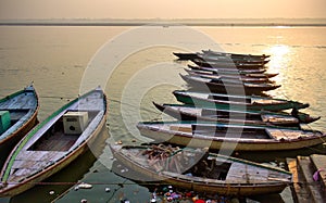 Varanasi, India: Bunch of old wooden colorful boats docked in the bay of Ganges river bank during sunset sunrise against foggy
