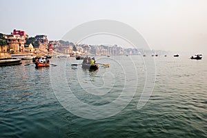 Varanasi, India: Tourist and pilgrim sightseeing on wooden boats in Ganges river against Ghat and Banaras