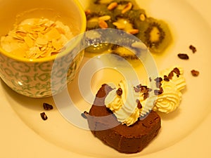 A variation of desserts served on a white plate: Chestnut chocolate terrine, marinated kiwi, and a vegan frangipane.