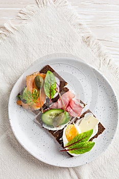 Variation of healthy open sandwiches on Pumpernickel bread with vegetables, salmon, ham, herbs and soft cheese