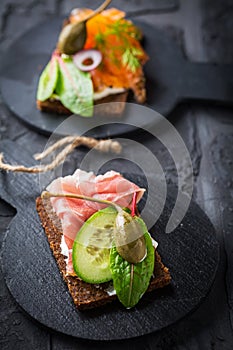 Variation of healthy open sandwiches on Pumpernickel bread with vegetables, salmon, ham, herbs and soft cheese