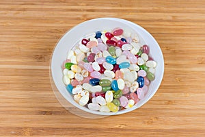 Varicolored jelly beans in bowl on wooden surface, top view