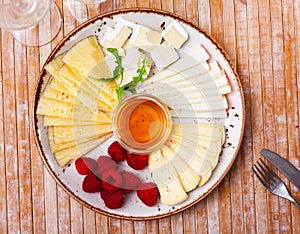 Varieties of cheese sliced and served with honey and raspberries