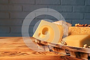 A variety of aged cheeses in a substrate on a wooden table against a brick wall