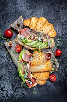 Variety of aperitifs Croissant sandwiches with jamon ham serrano paleta iberica, blue cheese, avocado, microgin on blue background