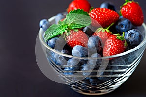 Variety of berries in a glass bowl on black background.