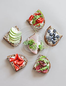 A variety of breakfast, tapas, snack sandwiches - with avocado, cream cheese, ham, berries, salami, cherry tomatoes on a light