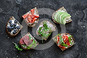 A variety of breakfast, tapas, snack sandwiches on a dark background - with avocado, cream cheese, ham, berries, salami, cherry