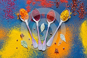 A variety of bright spices with spoons on a blue background. View from above.