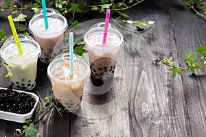 Variety of bubble tea in plastic cups with straws on a wooden ta