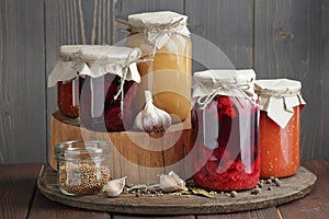 Variety of canned vegetable food: conserved beetroot, tomato paste, preserved bean, jam, pickles on wooden rustic background