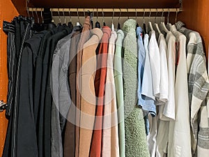 Variety of casual teenage girl clothes of different colors on hangers in wooden wardrobe