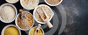 Variety of cereal flakes rice, millet, buckwheat, oatmeal. Superfood in white ceramic bowls on dark old concrete background. Top