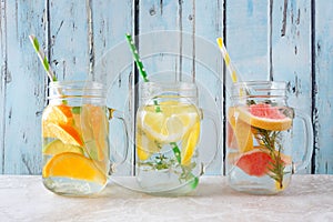 Variety of citrus infused detox water drinks in mason jars against blue wood