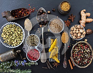 Variety of colorful spices and herbs on black stone background, top view