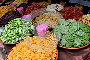 Variety of colorful sugared and dried fruits of: melon, kiwi and grapefruit with signs in Spanish indicating each one.