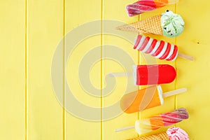 Variety of colorful summer popsicles and ice cream desserts. Side border on a yellow wood background.