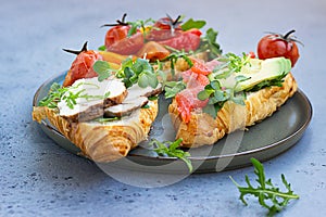 Variety of croissant sandwiches with grilled pepper, tomatoes, smoked salmon, turkey, avocado and arugula served with micro green