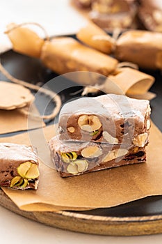 A variety of different nutty nougat in dark chocolate with roasted hazelnuts cut open to show the nougat mix on a wooden