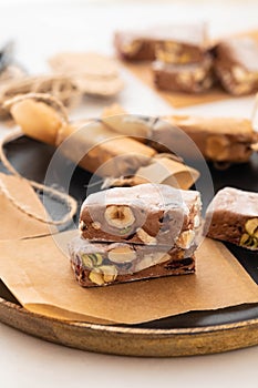 A variety of different nutty nougat in dark chocolate with roasted hazelnuts cut open to show the nougat mix on a wooden