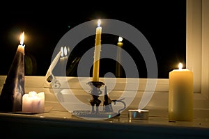 A variety of different shaped candles burning on a white windowsill