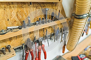 Variety of different tools such as standard pliers, screwdriver, and nails hanging on a wall. Carpenter workshop