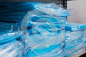 A variety of disposable medical blue garments in bags on the shelves. Factory disposable clothing.